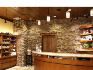 A curved wooden home bar next to a tan stone wall and shelves. Perfect 6 Marketing represents home design companies.