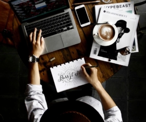 A person draws and also works on the computer with coffee to the right.