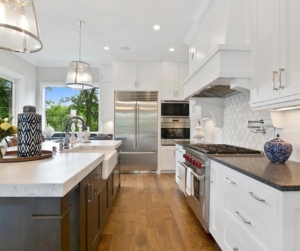 A dual toned kitchen with wood floors and glass pendant lights.