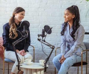 Two women casually talking into mics for a podcast.
