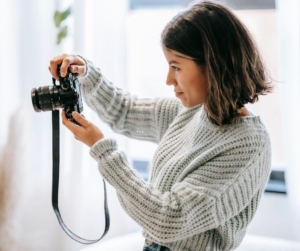 A woman with short brown hair photographs a white room.