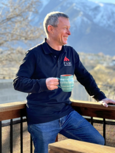 Near Me custom logo apparel gear shirts man holding a cup of coffee leaning on a railings 