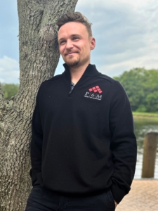 Man leaning against a tree wearing a black Timber zip near me custom apparel